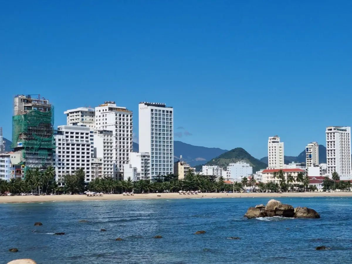 A rocky outcrop in shallow blue water in front of a row of white high-rise hotels