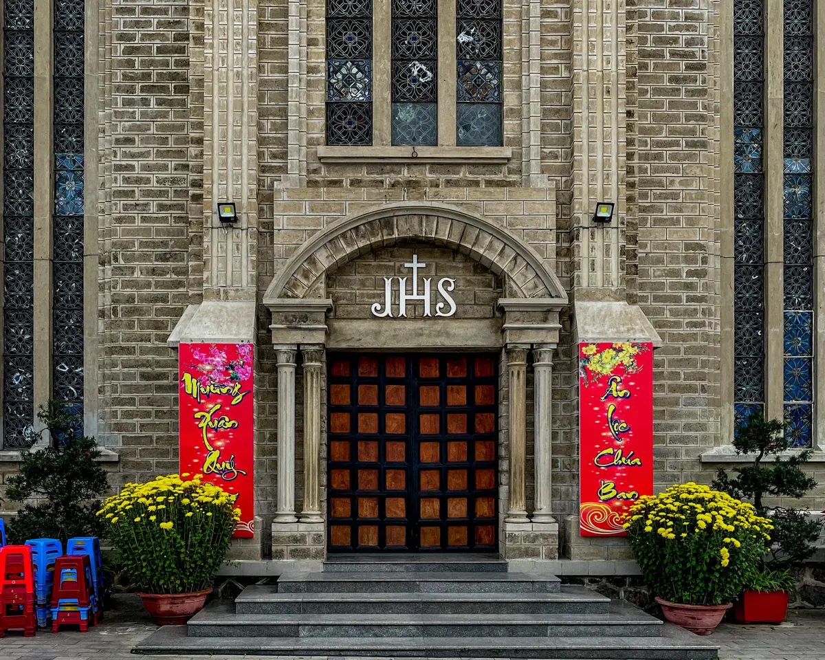 Cathedral entrance with arched wooden door, red banners and pots of yellow flowers