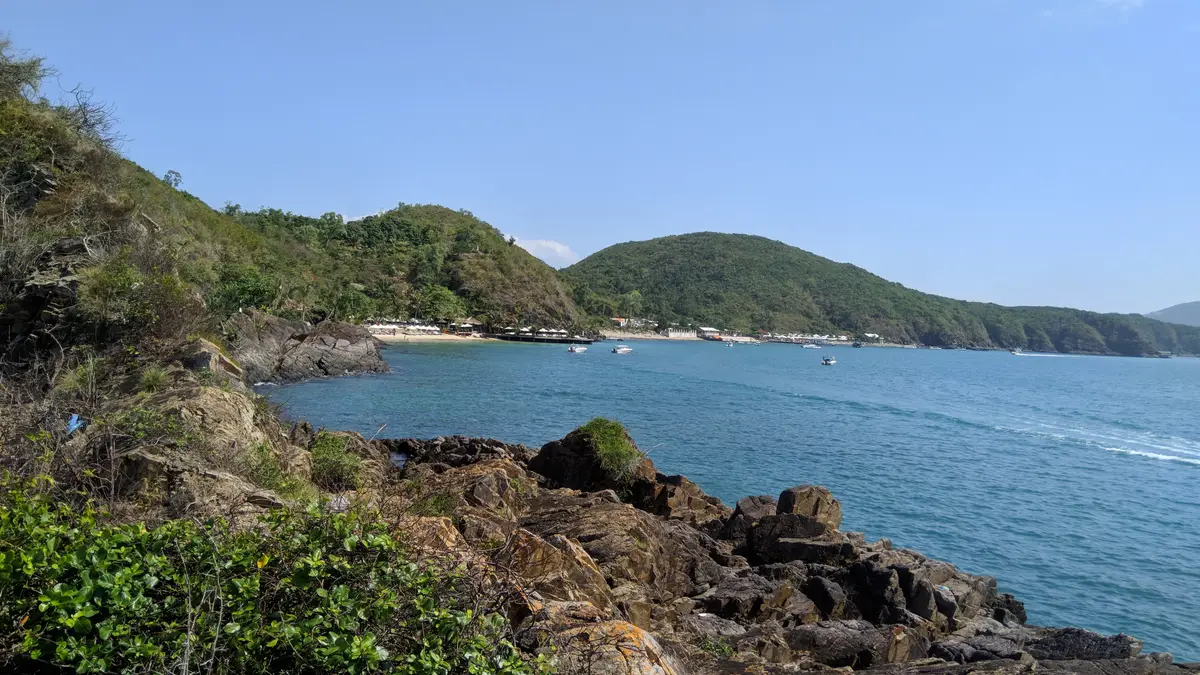 View across a bay from a rocky headland with green hills and a distant beach
