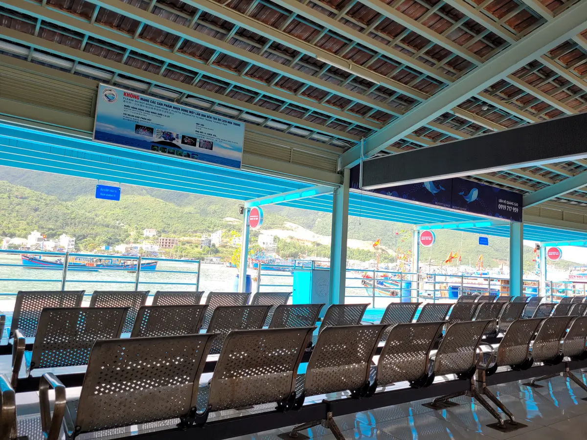 Rows of metal benches in a covered waiting hall facing the harbour
