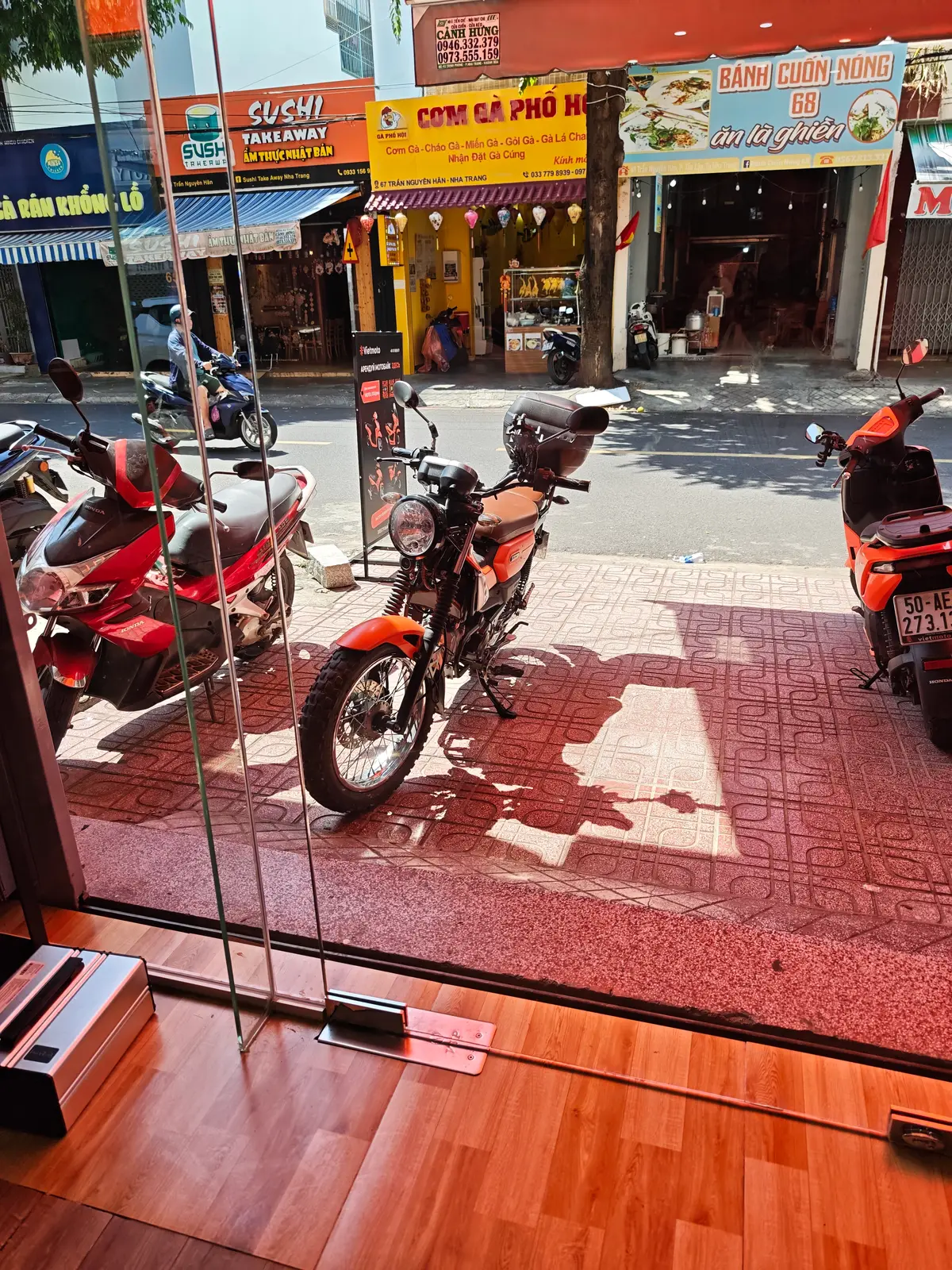 Orange motorbikes parked in a row outside a shop on a tiled pavement