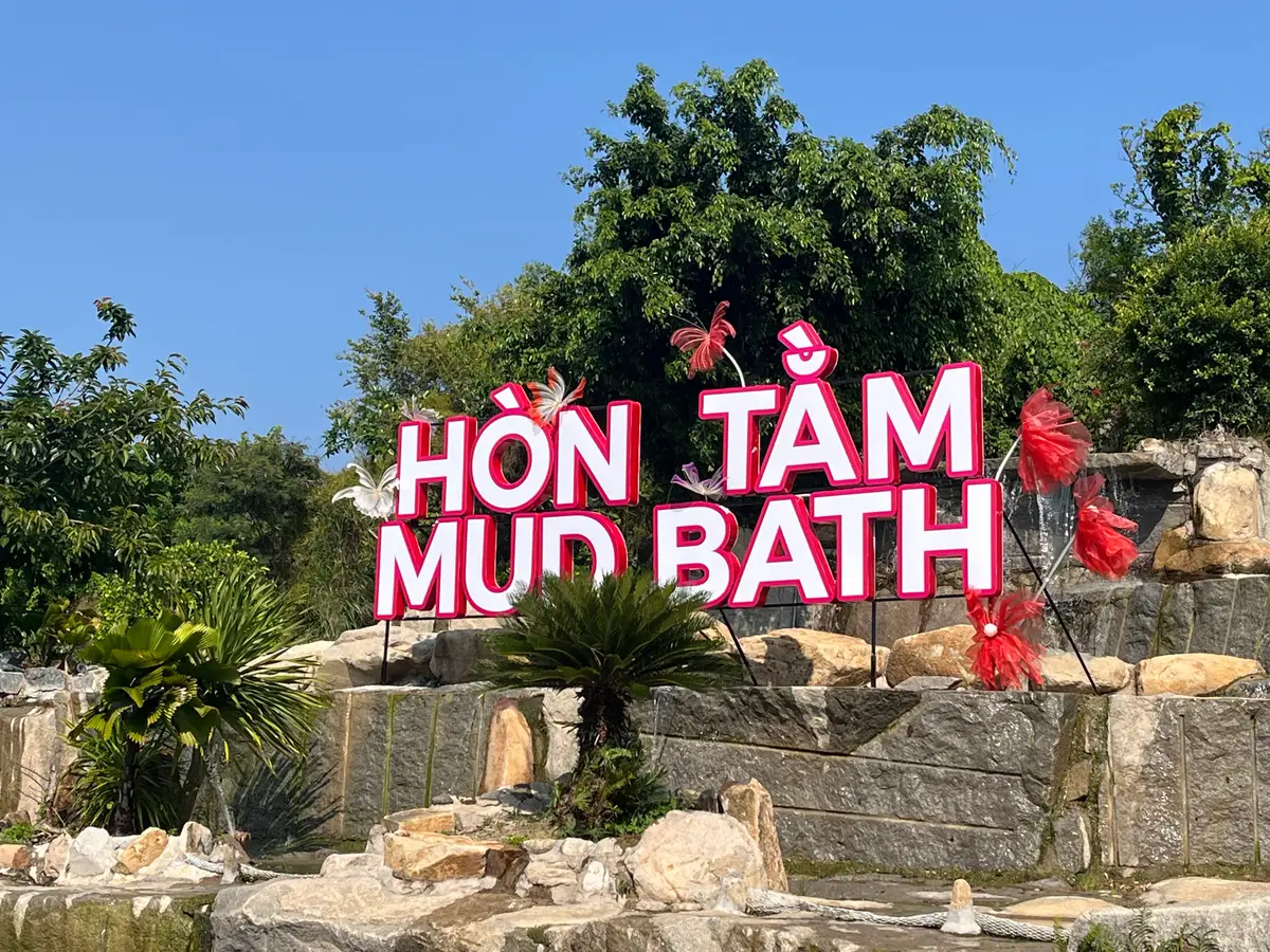 Pink Hon Tam Mud Bath sign among palms and rocks