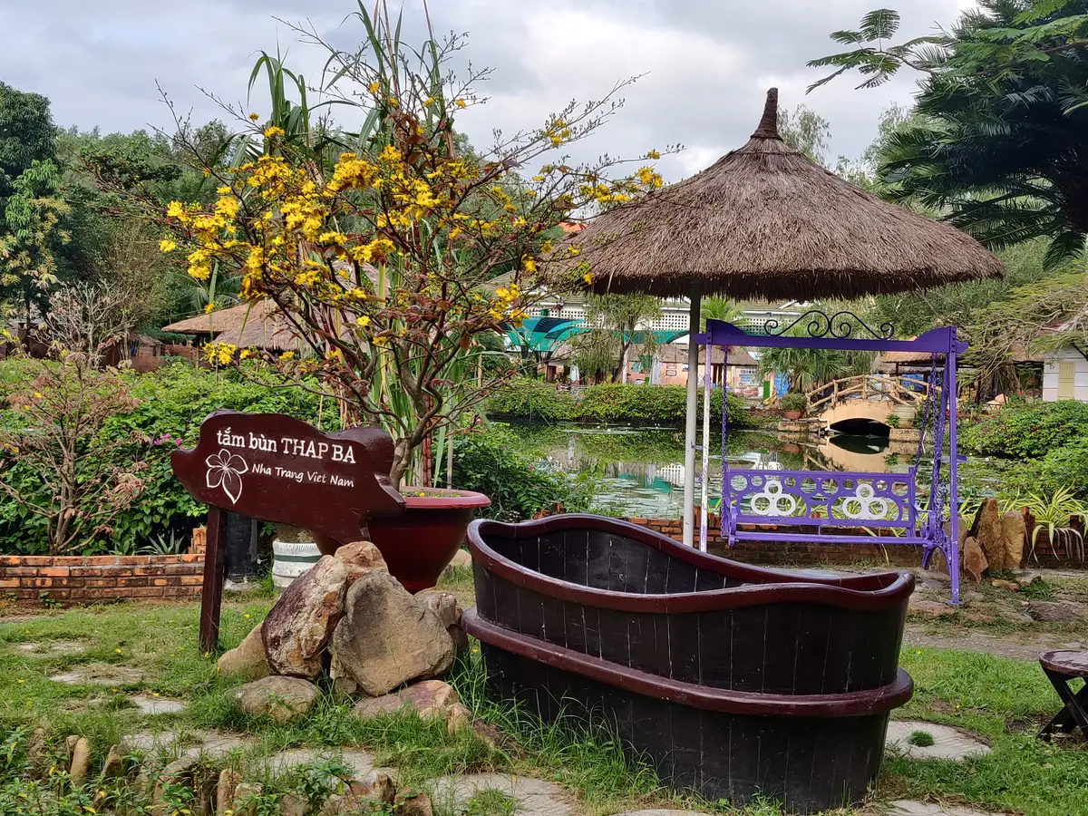 Wooden bathtub on a stone path beside a sign and a thatched parasol