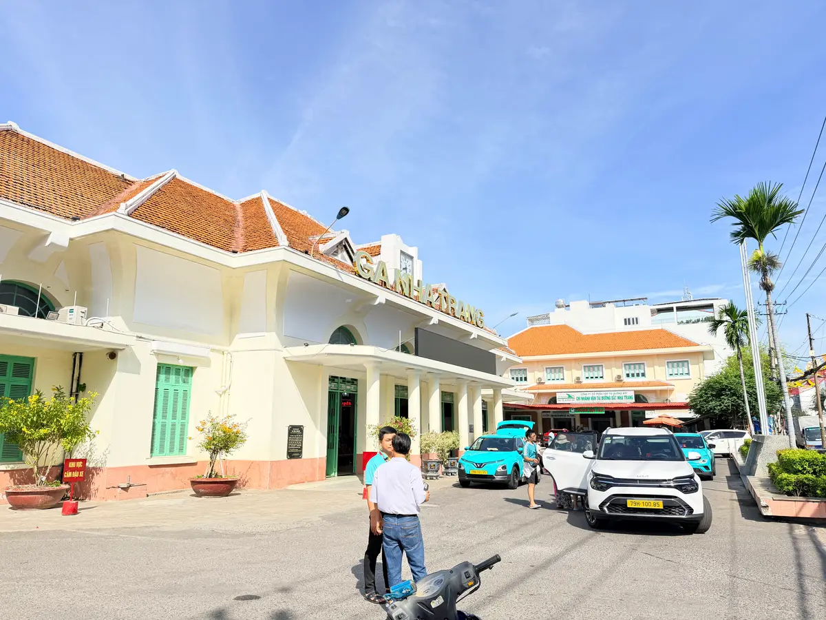 Cream station building with an orange tile roof and cars parked in front