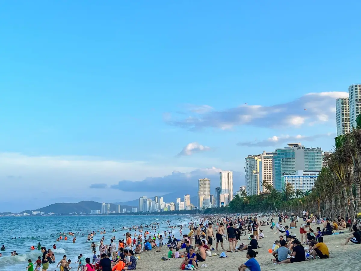 Crowded swimming beach in Nha Trang under blue sky with hotel towers behind