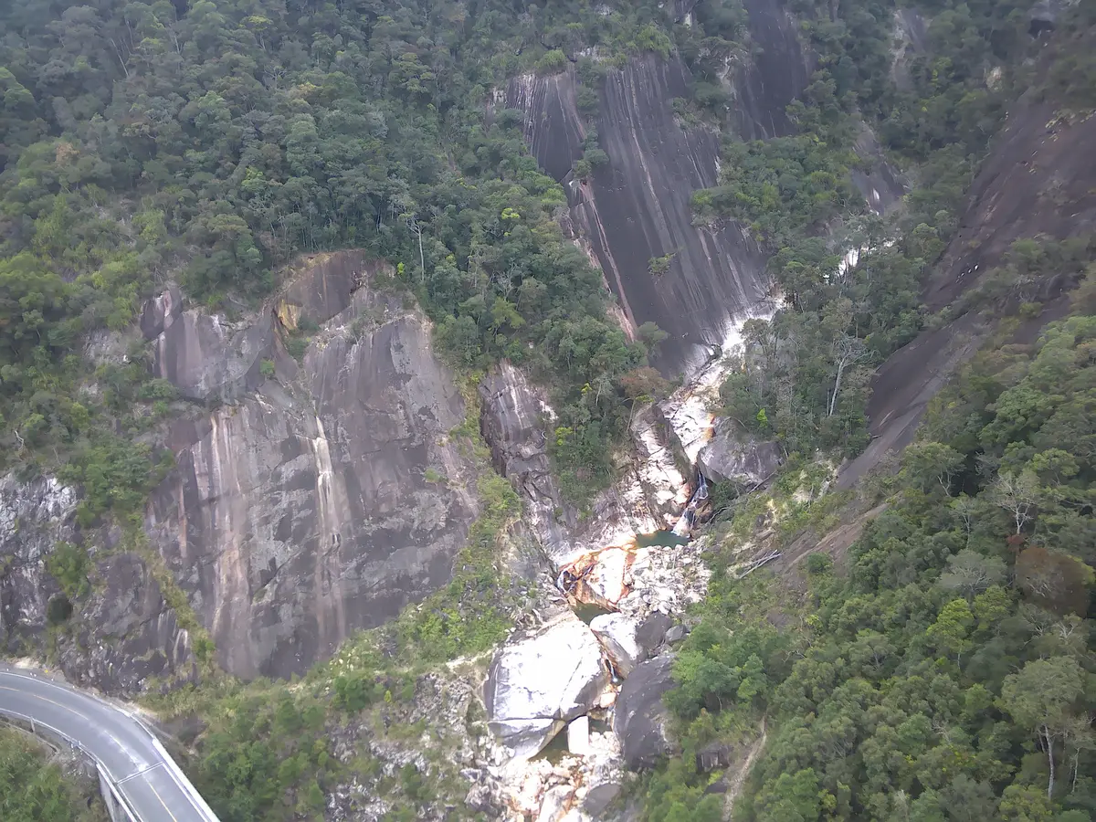 Waterfall streaming down a grey granite cliff beside a curve of the road