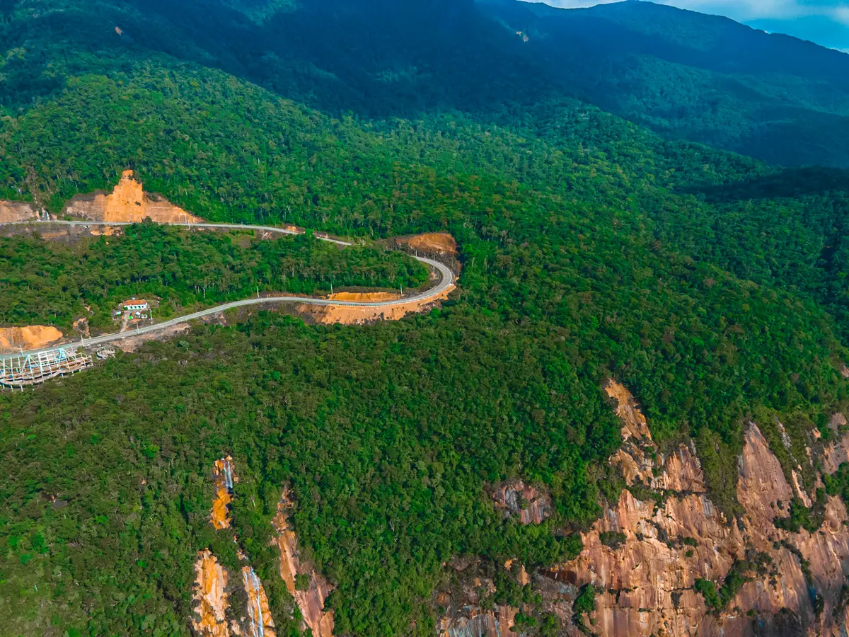 Road winding in tight bends down a green mountainside with orange cut banks