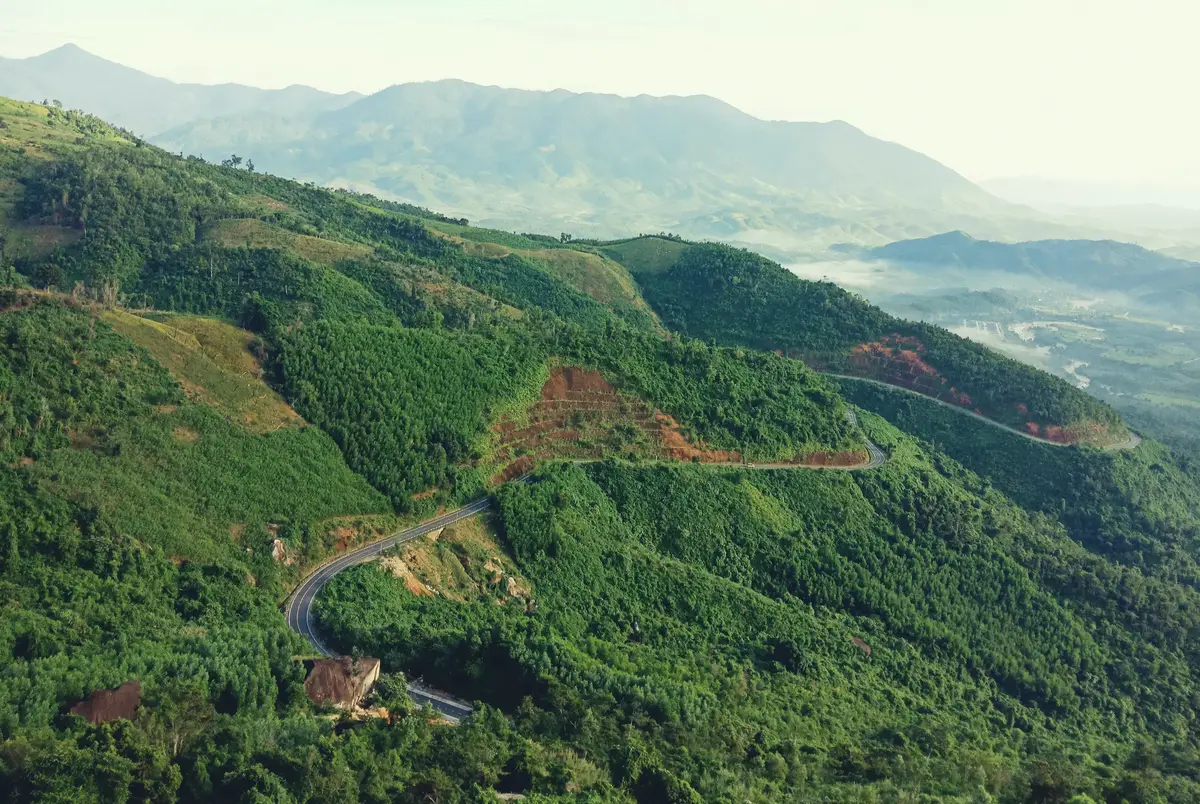 Narrow road switchbacking across a green hillside above a misty valley