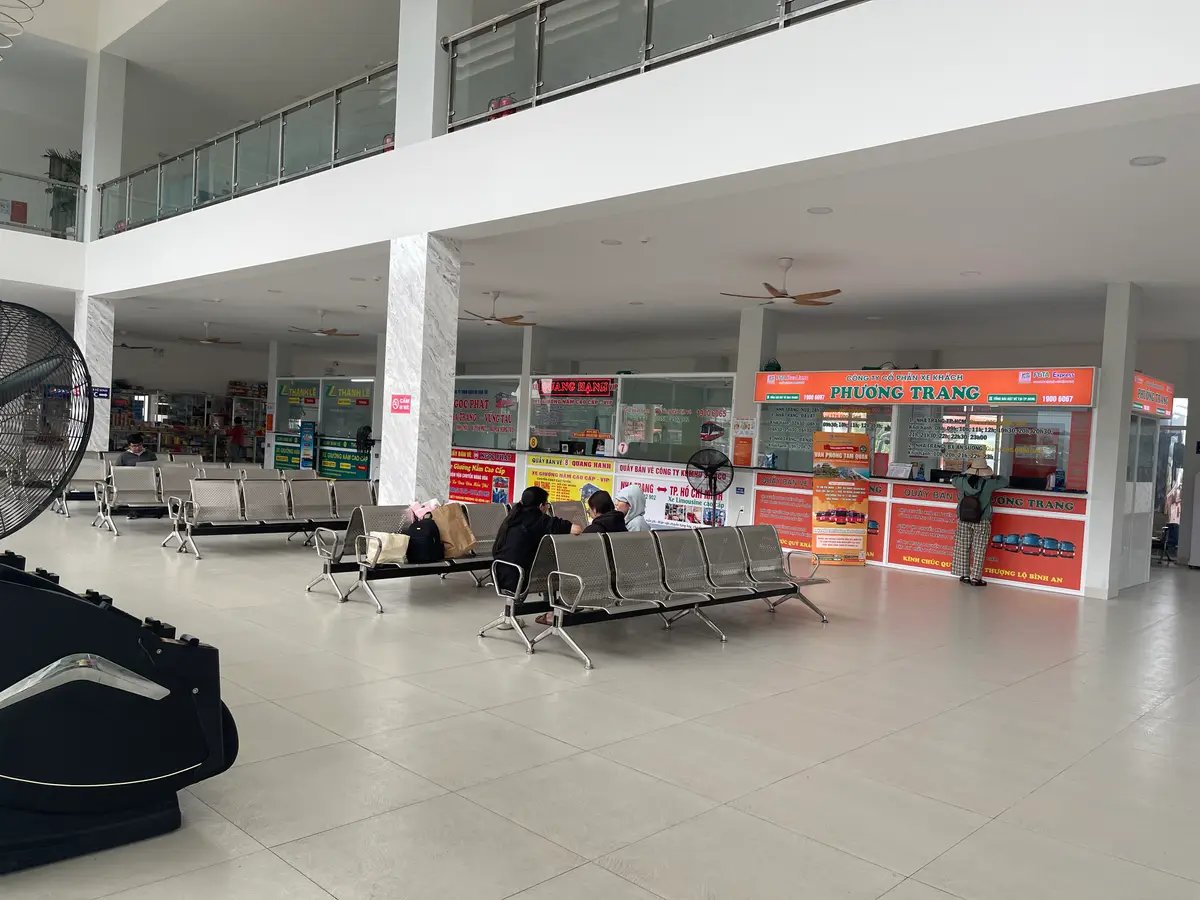 Open ticket hall with grey benches and orange ticket booths under a high ceiling