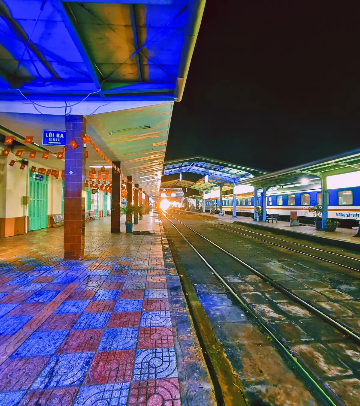 Platform at night with a blue train arriving beside a tiled walkway