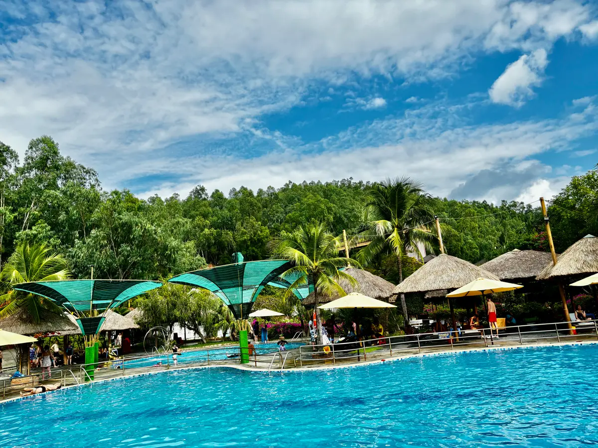 Blue swimming pool with thatched parasols and trees at a hot spring park