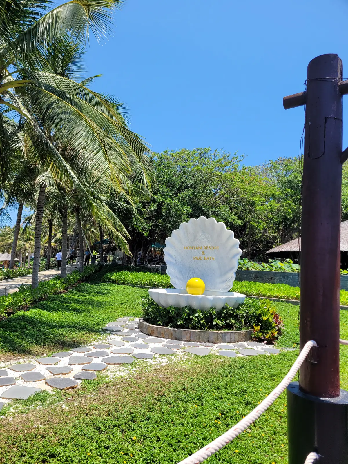 White shell sculpture with a golden pearl in a garden of palms