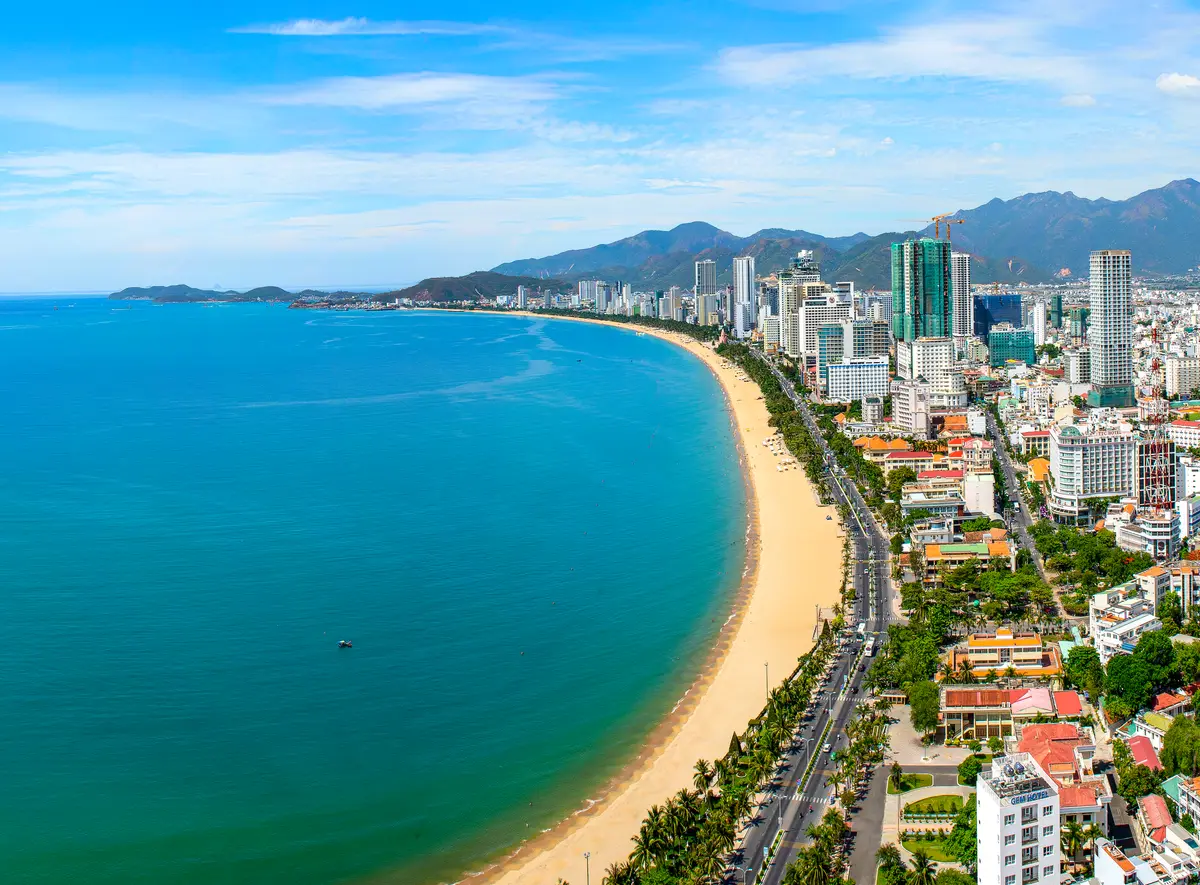 Aerial view of a long curved city beach with turquoise water and a coastal road