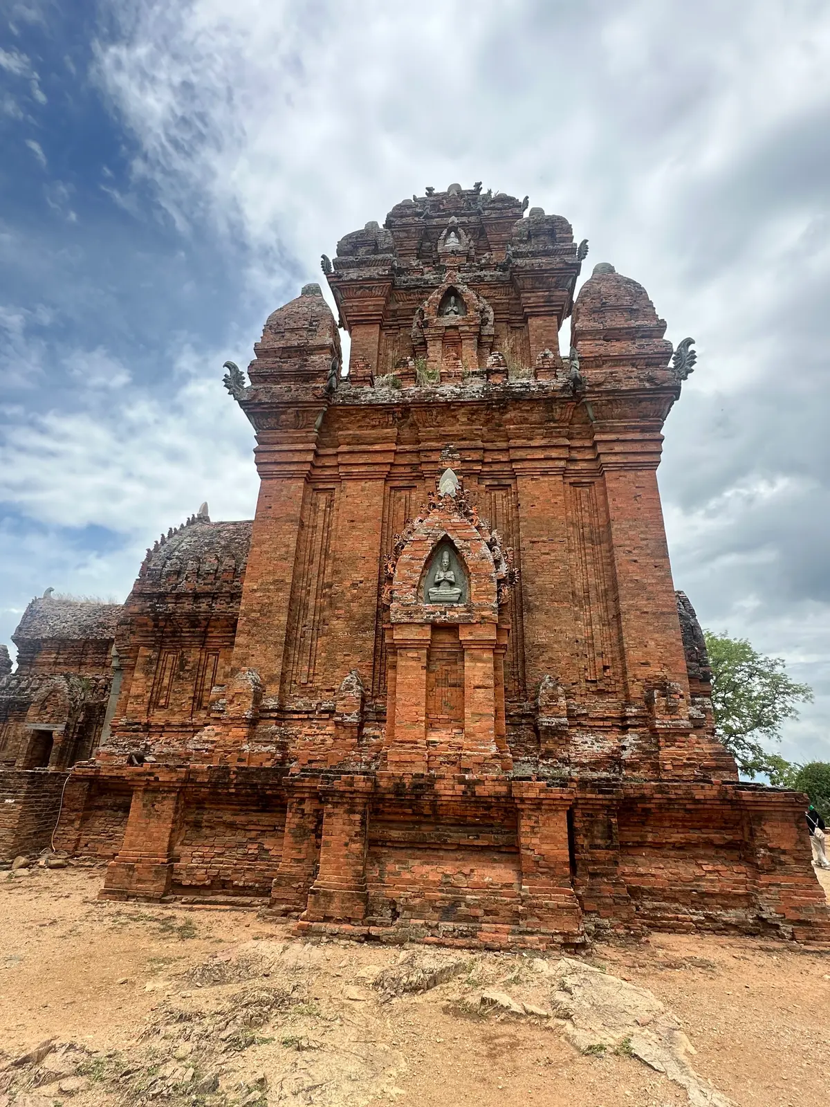 Close view of a tall red brick tower with carved niches and a pointed stepped roof