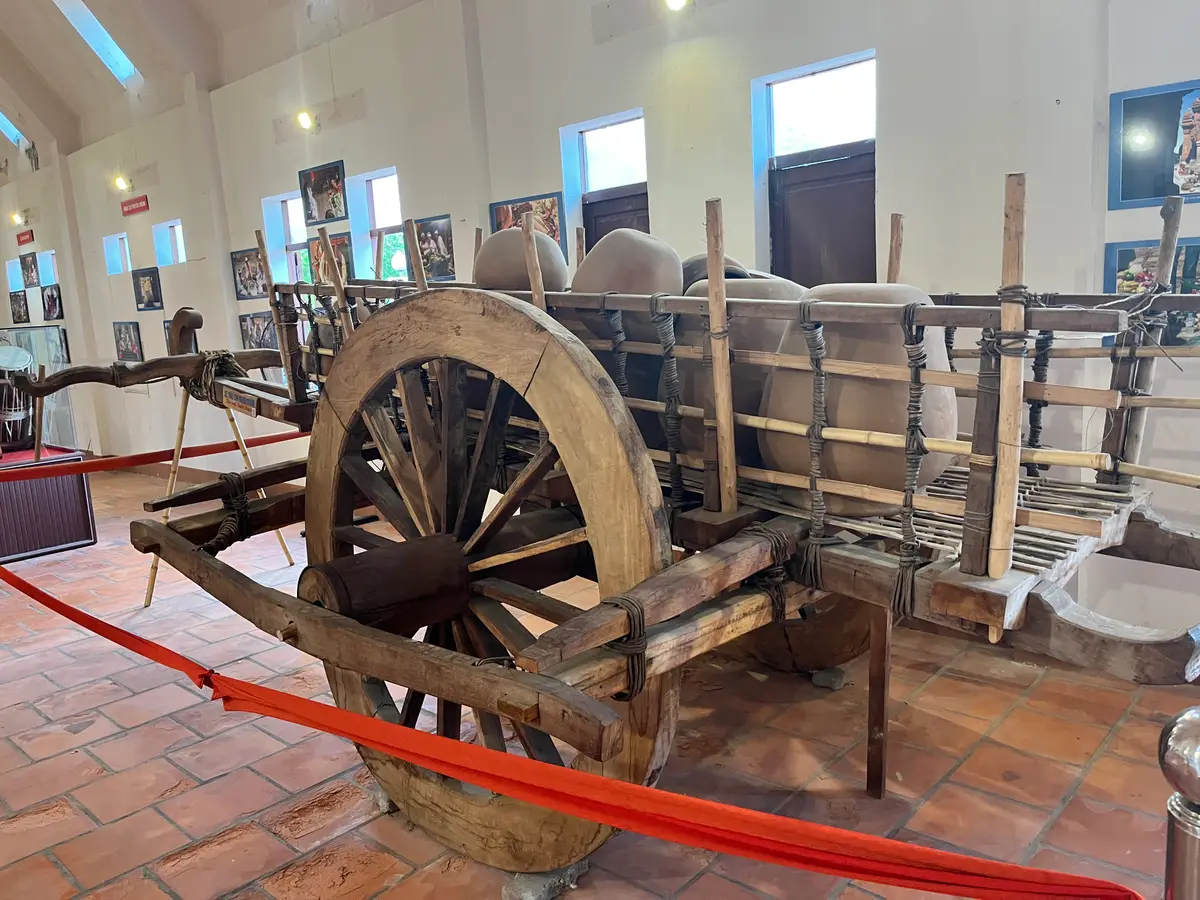 Wooden ox cart and large grinding stones displayed inside a tiled museum hall