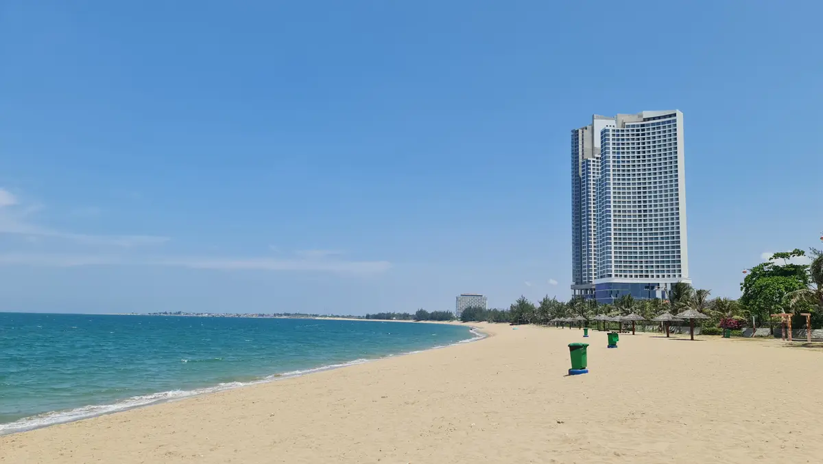 Wide sandy beach with turquoise water and a tall hotel tower in the distance
