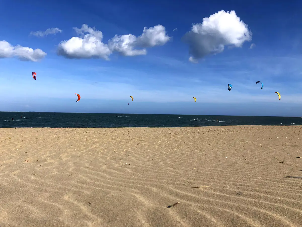 Rippled sand in front of the sea with colourful kites flying above kite surfers