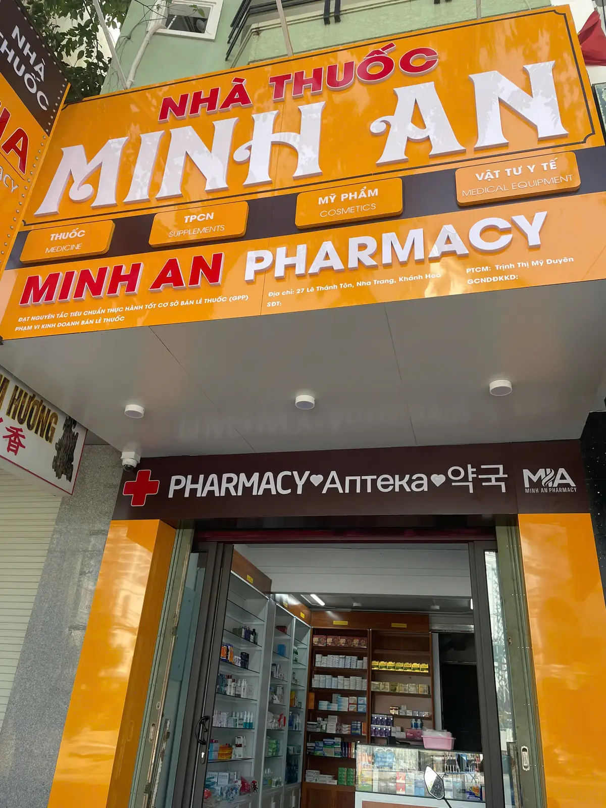 Orange pharmacy shopfront with a red cross and the word Pharmacy in several languages