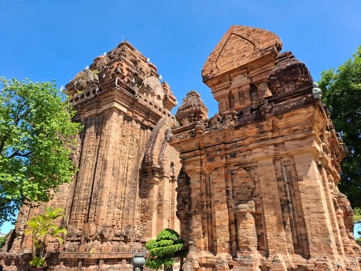 Two red brick Cham towers with carved doorways seen from a courtyard under a blue sky