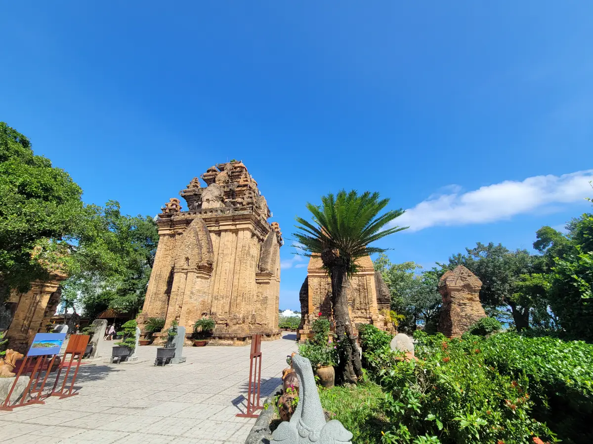 Stone path leading toward the Cham towers under a tall palm and blue sky