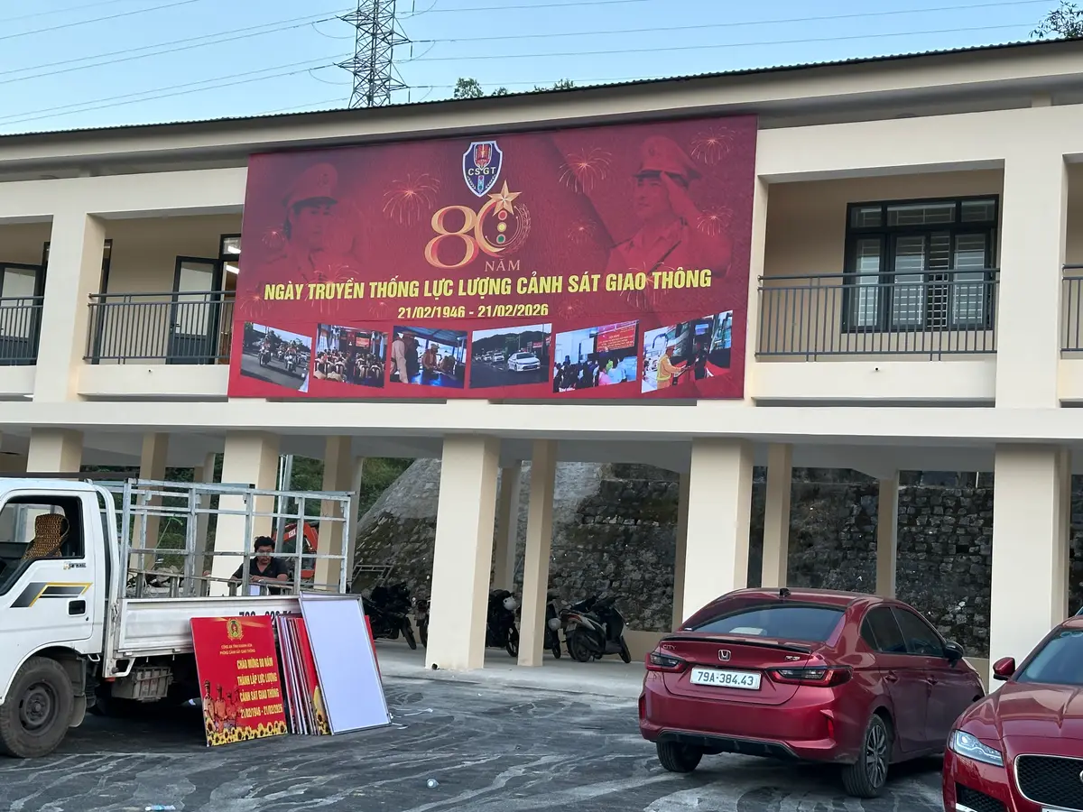 Two-storey office building with a red banner on the upper wall and a pickup truck and a red car parked in front.