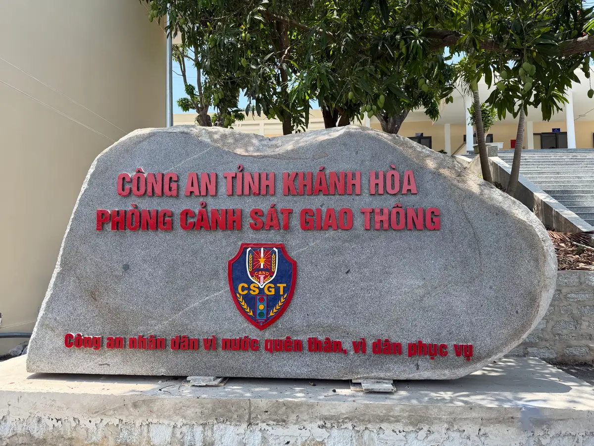 Large stone sign with the red lettering of the Khanh Hoa provincial police and the traffic police department and an emblem.
