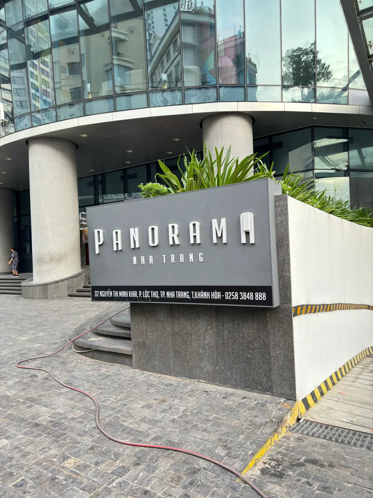 Stone sign with the building name Panorama Nha Trang at the foot of a tower, with a planted bed beside it