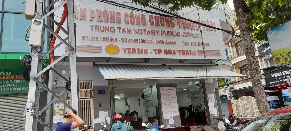 Shopfront of a notary public office with a large sign, a striped awning and notices posted on the glass