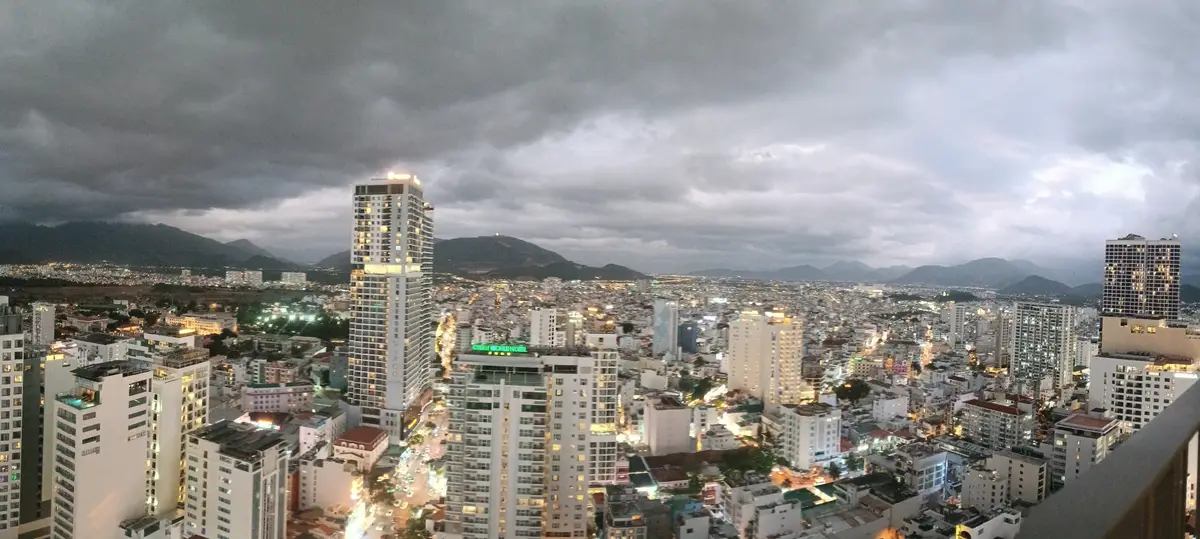 View over Nha Trang from a high floor with apartment towers, low buildings and hills under a cloudy sky