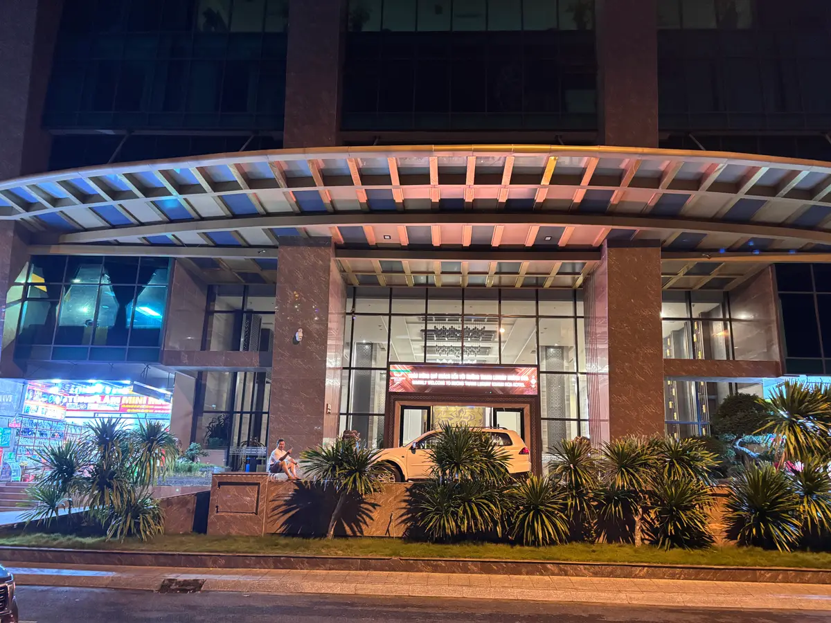 Glass entrance of a tower with a long canopy, palm plants and a paved forecourt