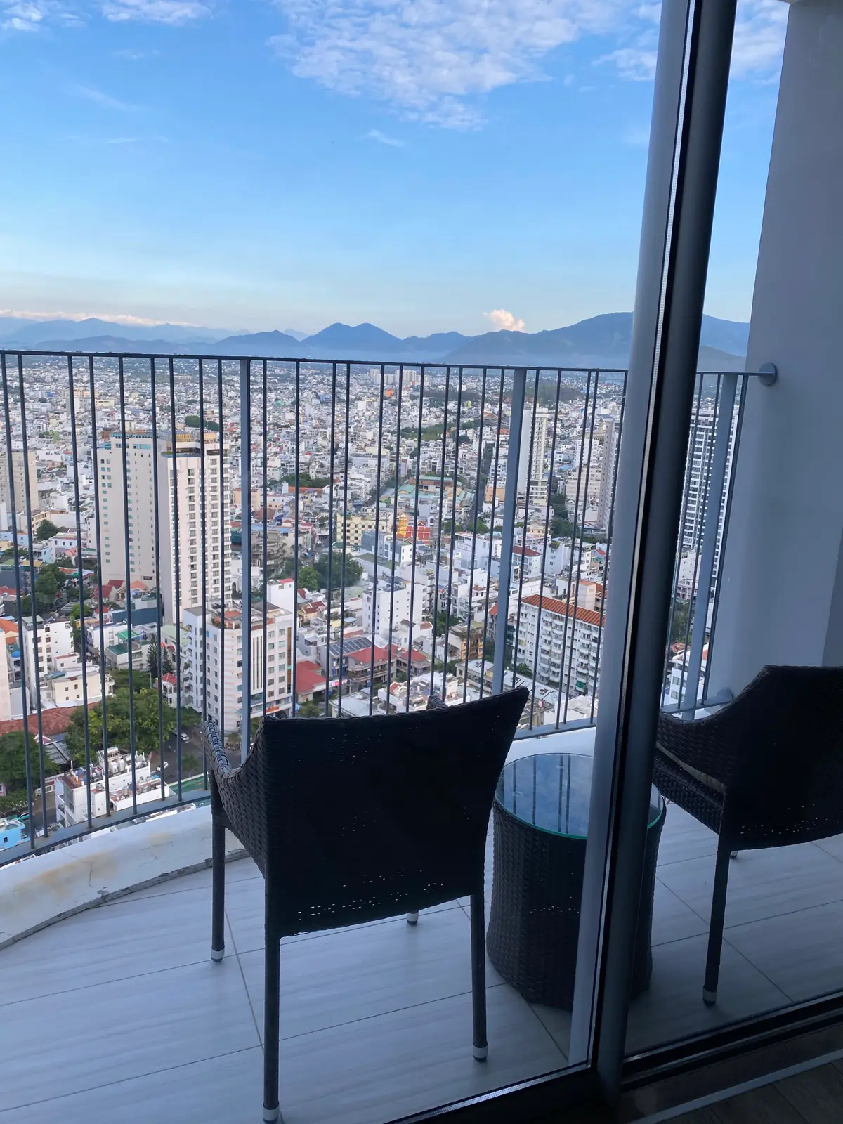 Apartment balcony with black chairs and a glass railing looking over the city rooftops towards the mountains