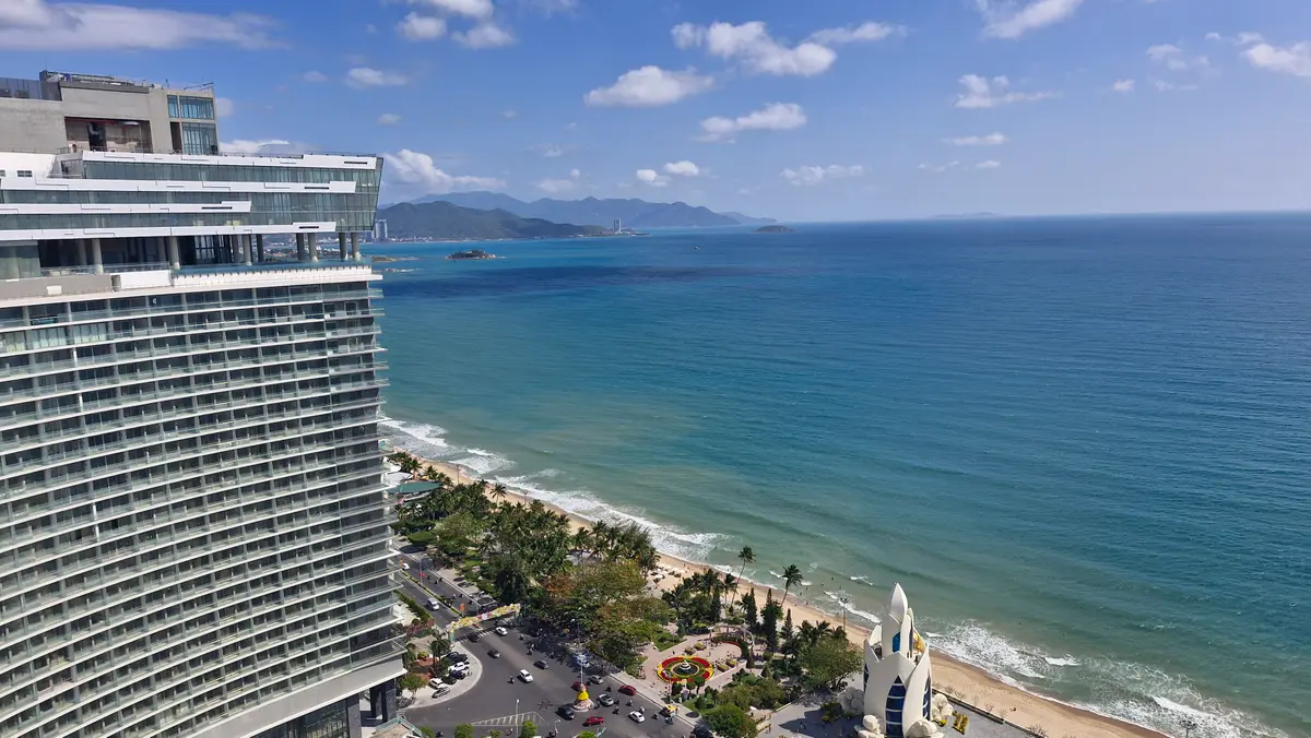 Tall apartment tower beside a wide beach and a blue sea under a clear sky