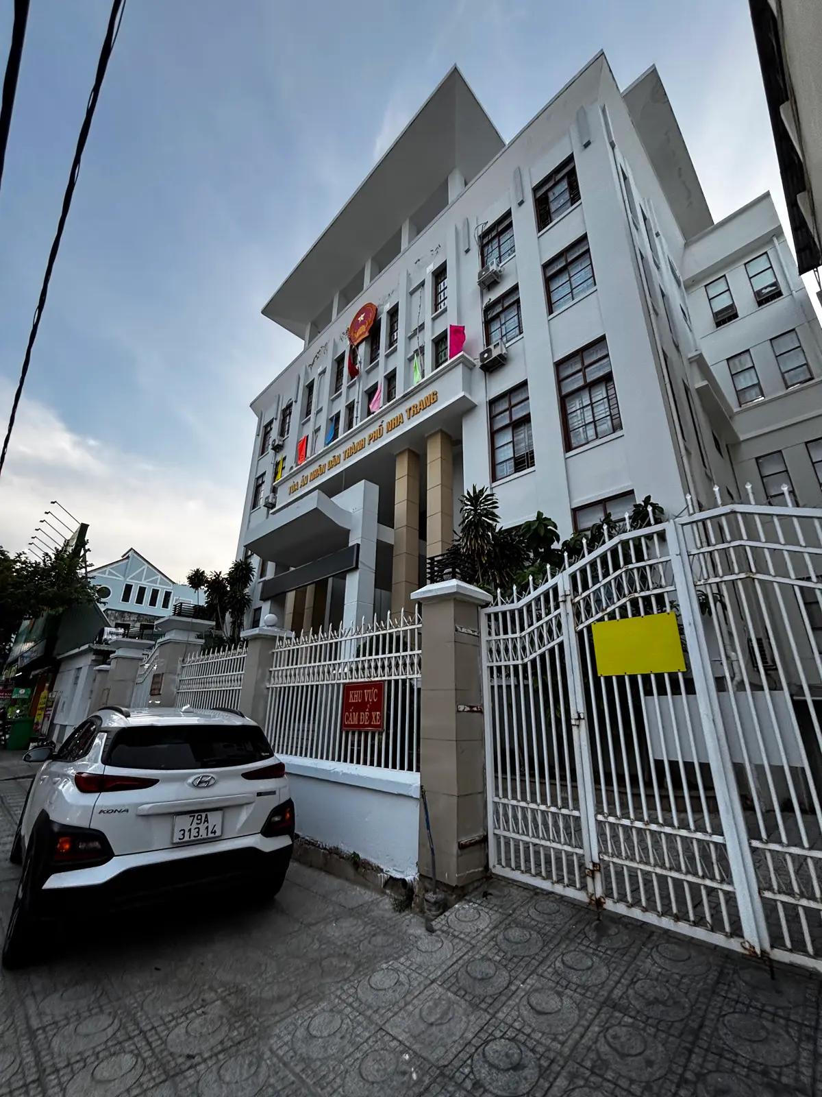 Corner of a white court building with a covered entrance, a metal gate and a parked white car