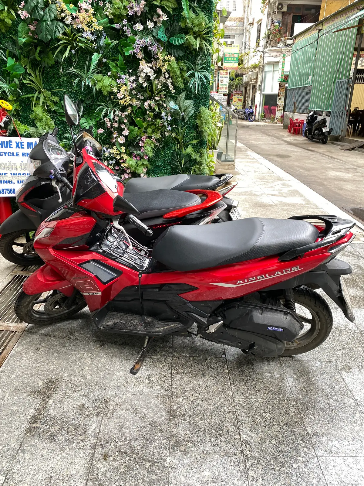 Red Honda Air Blade scooter parked on a tiled pavement next to another scooter