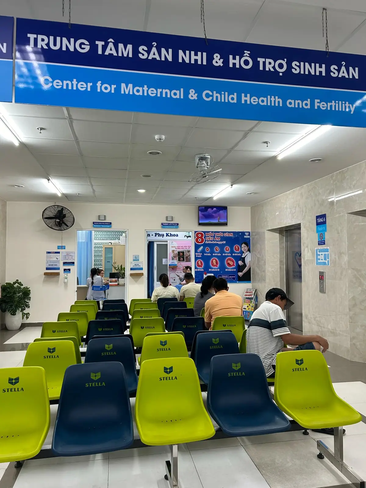Hospital waiting area with rows of green and blue chairs and a reception counter