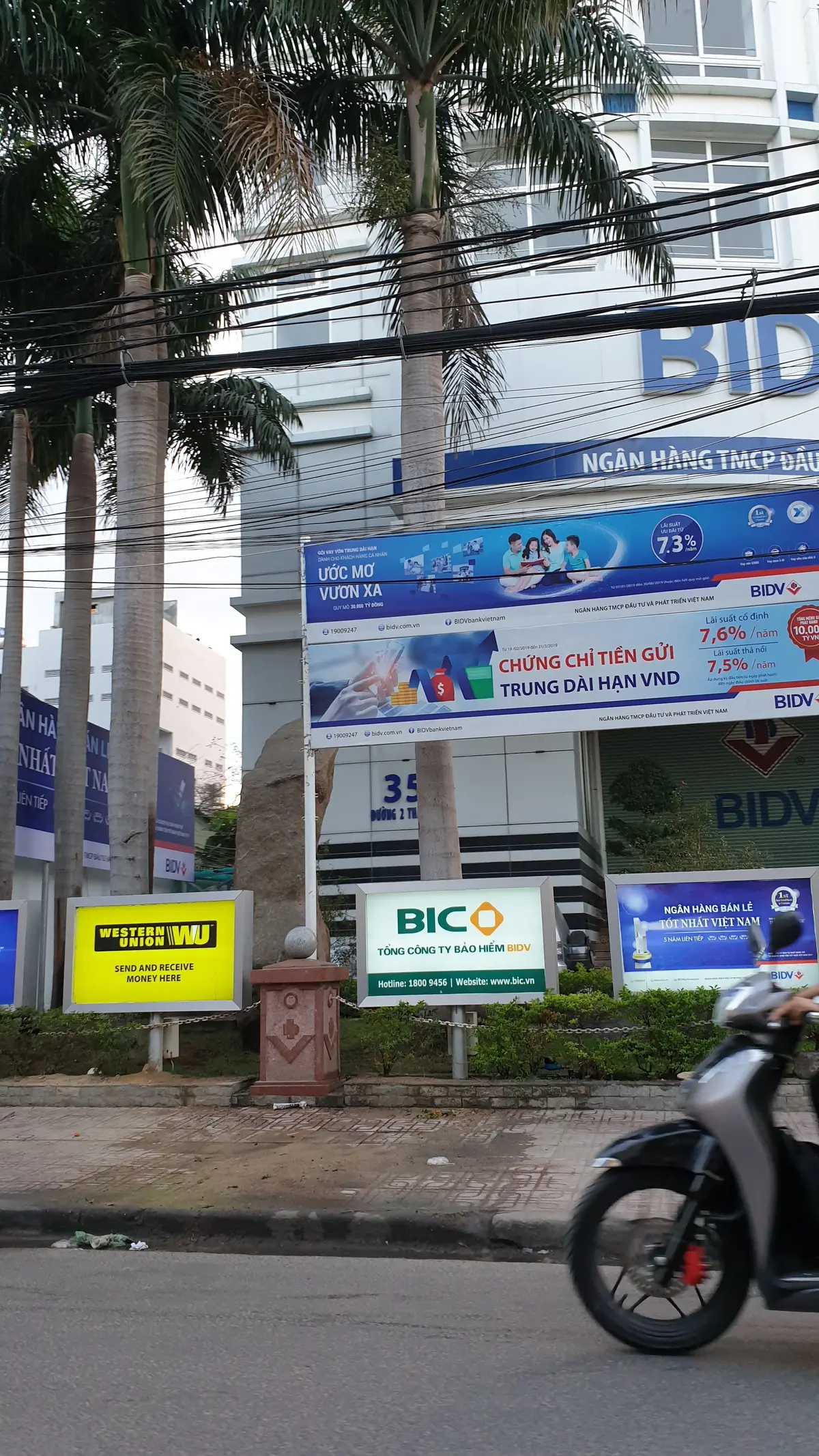Roadside billboard with a yellow Western Union sign and an insurance logo in front of the bank building.