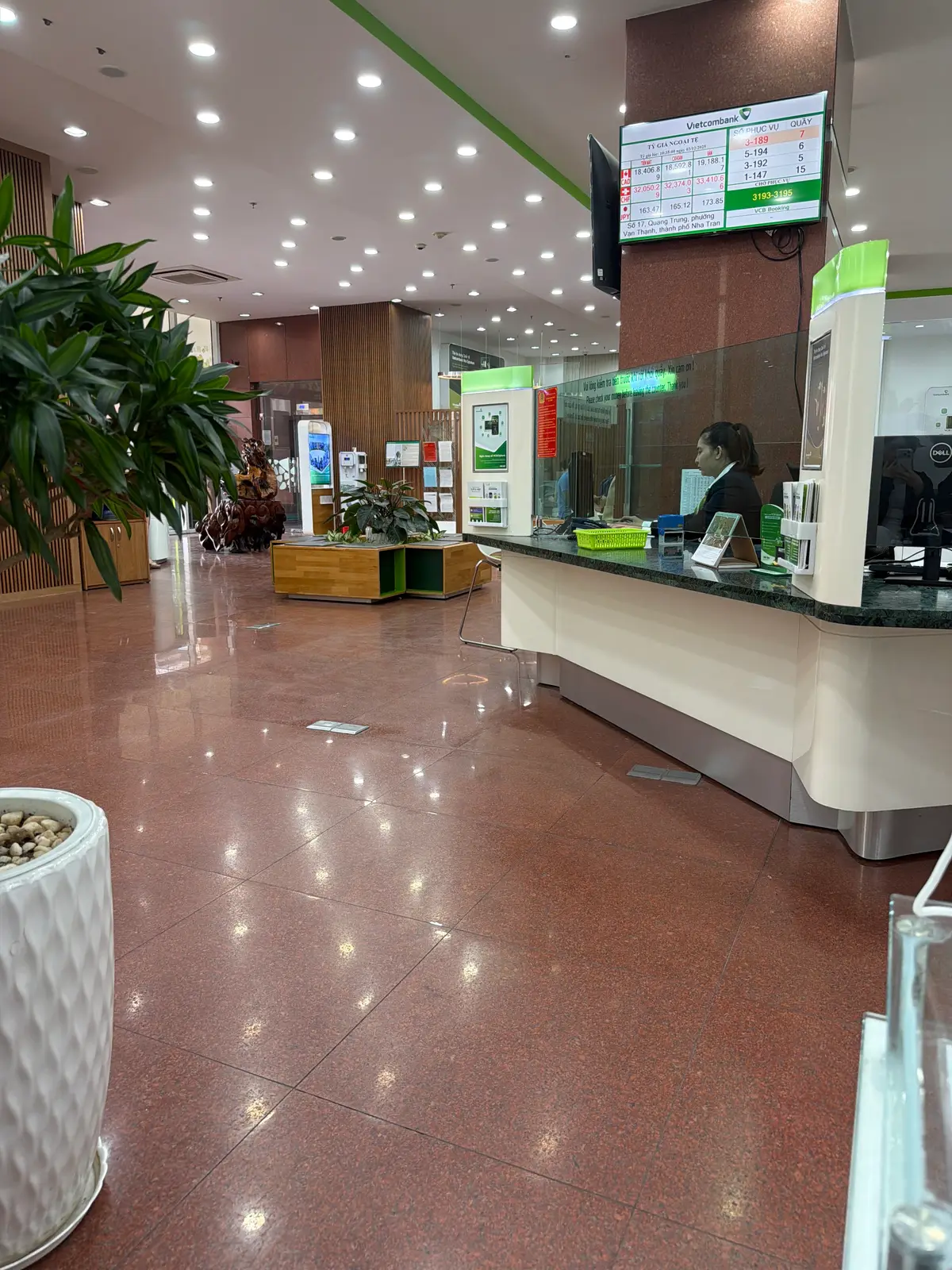Service counter inside the banking hall with a clerk behind a glass partition and the polished floor in front.