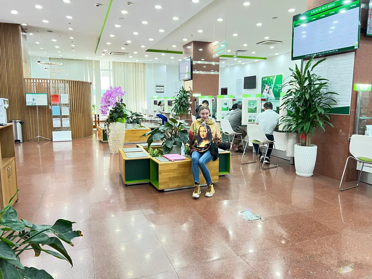 Banking hall with a polished floor, plants, seats and a customer waiting near the counters.