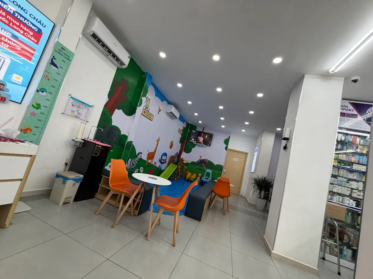 A bright waiting room with orange stools, a children's wall mural and a ceiling air conditioner.