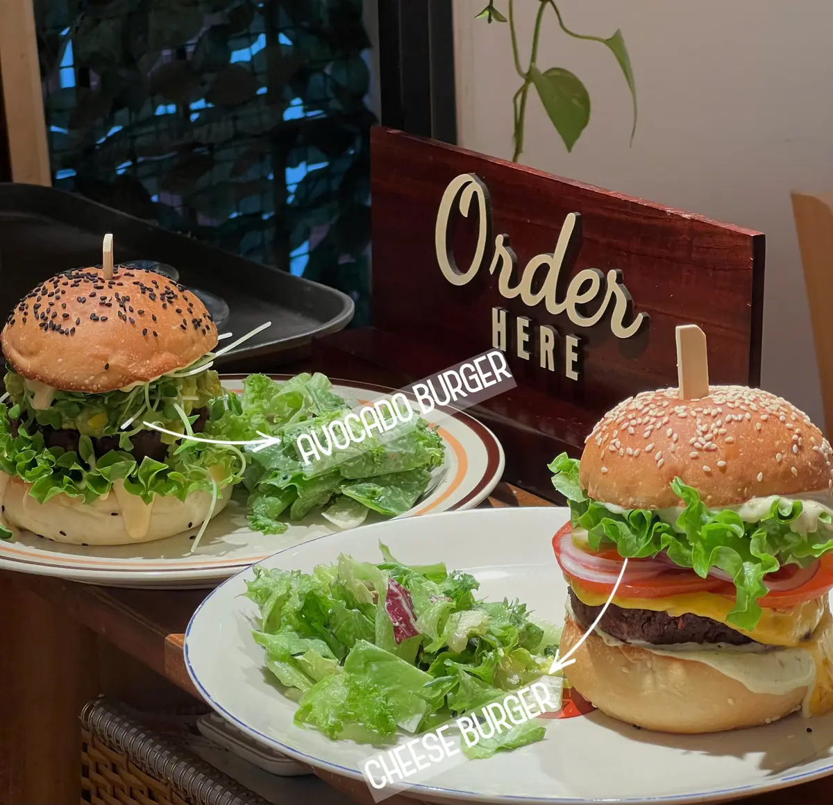 Two veggie burgers on plates beside a wooden Order Here sign