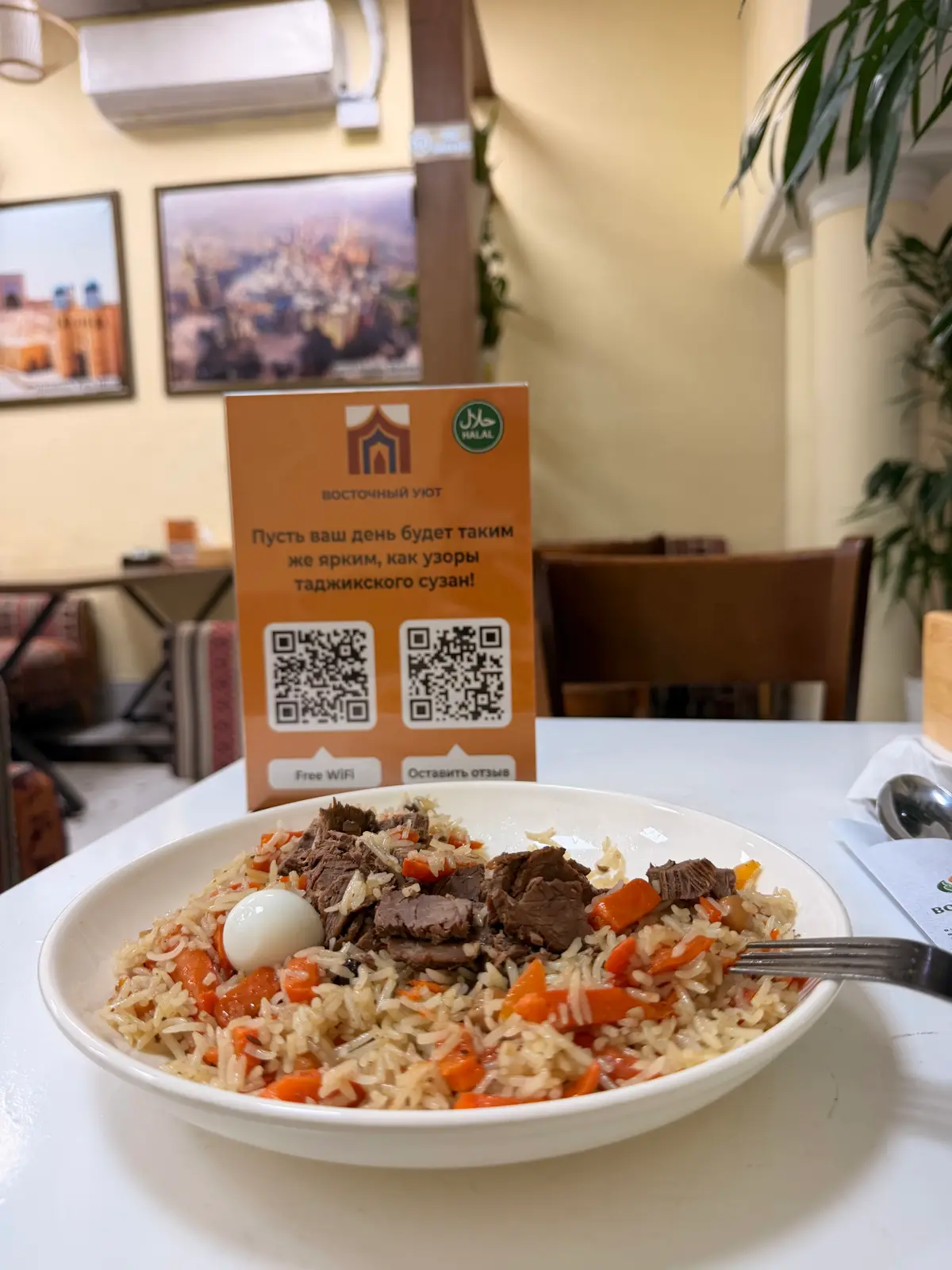 Plate of pilaf with beef and a boiled egg beside a table sign with two codes