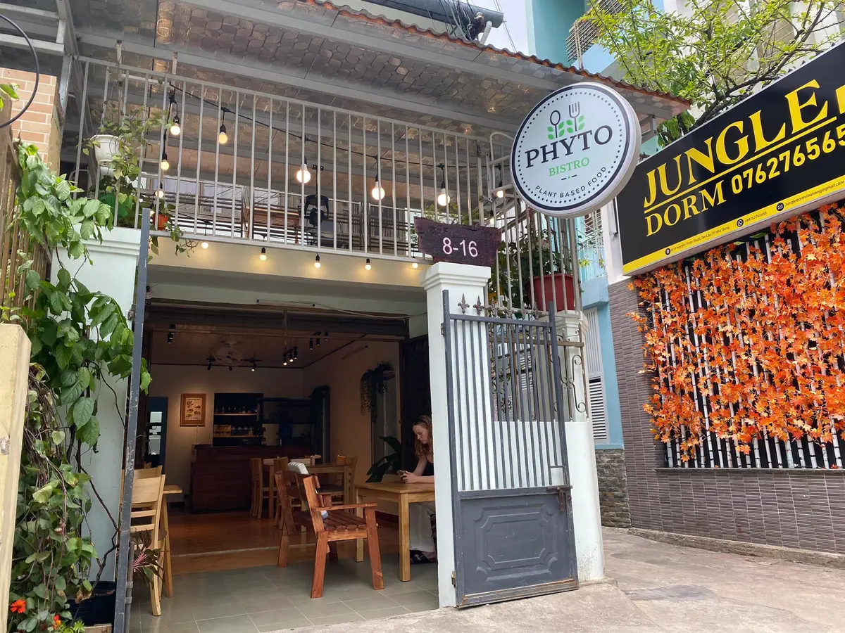 Narrow cafe entrance with a round Phyto sign, plants and a gate