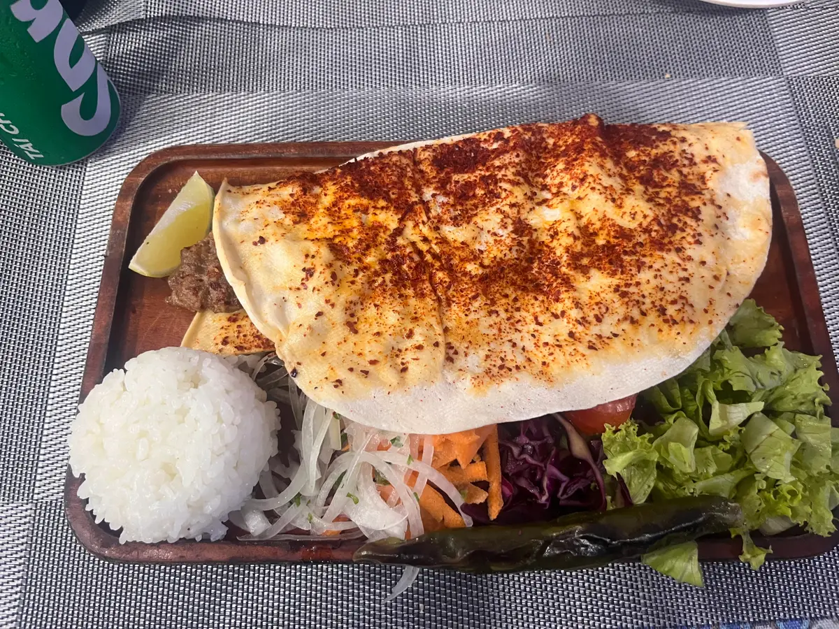 Turkish pide topped with melted cheese and spices beside rice and salad on a wooden tray
