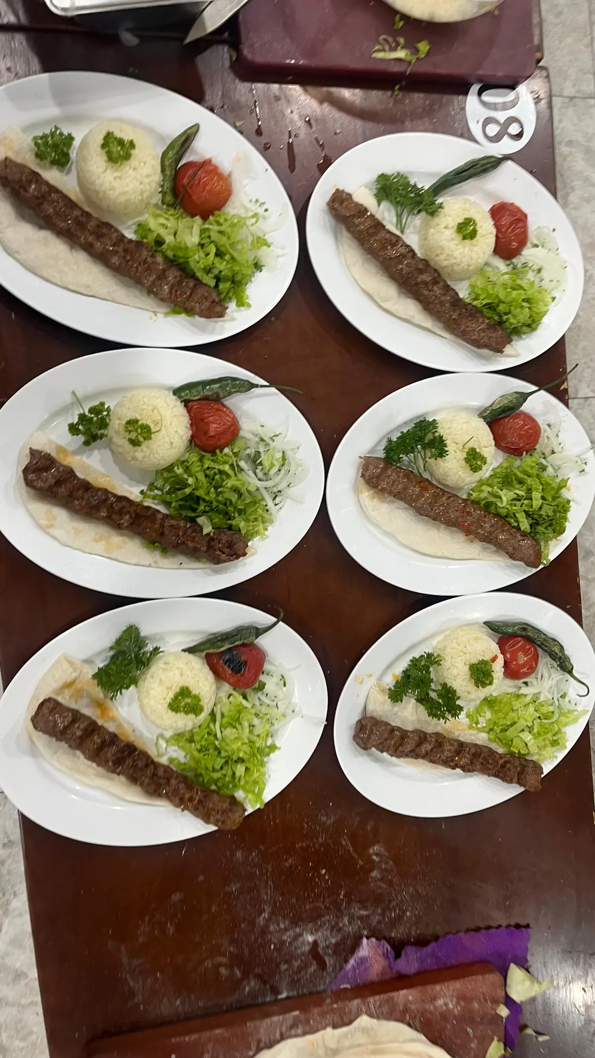 Four plates of Adana kebab on flatbread with rice, tomato and herbs