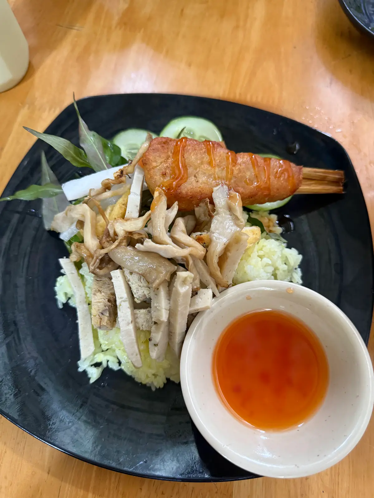 Black plate of sliced mushrooms and plant-based sausage beside a bowl of sweet chilli sauce