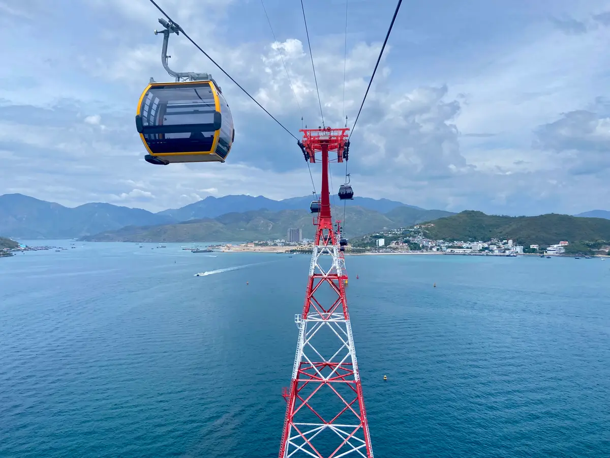 Red cable car pylon and a gondola over the bay with mountains in the distance