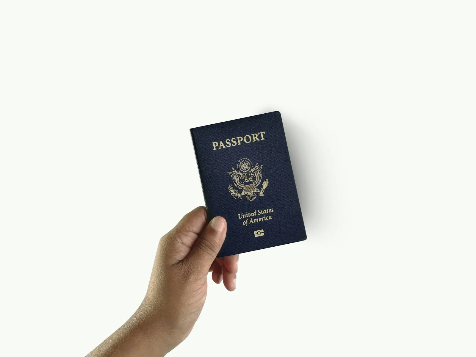 A hand holding a dark blue passport against a white background