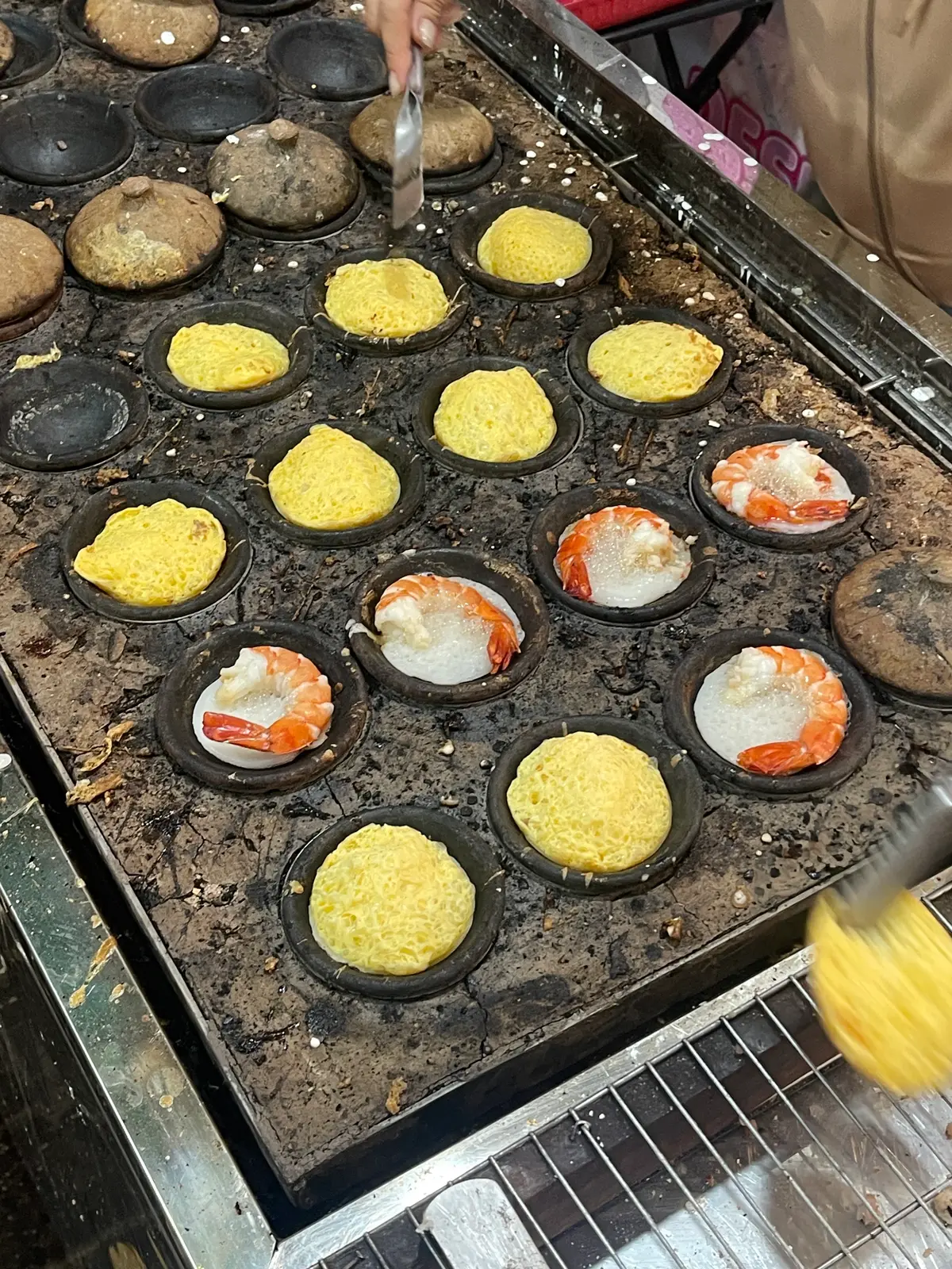 Cast-iron mould grill with rice pancakes baking, some topped with shrimp and others with egg yolk