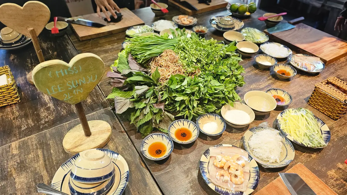 Wooden table covered with small bowls of sauces, noodles, herbs and toppings