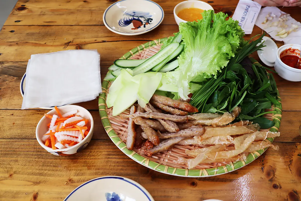 Round tray of grilled pork skewers with lettuce, herbs, cucumber and pickled carrot